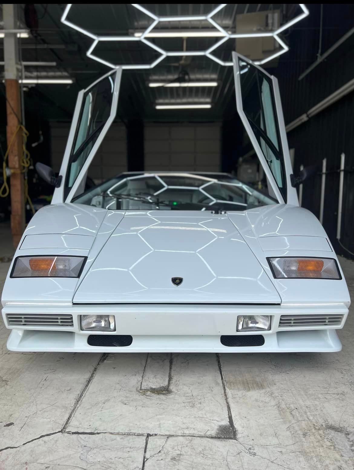 A white lamborghini with its doors open is parked in a garage.