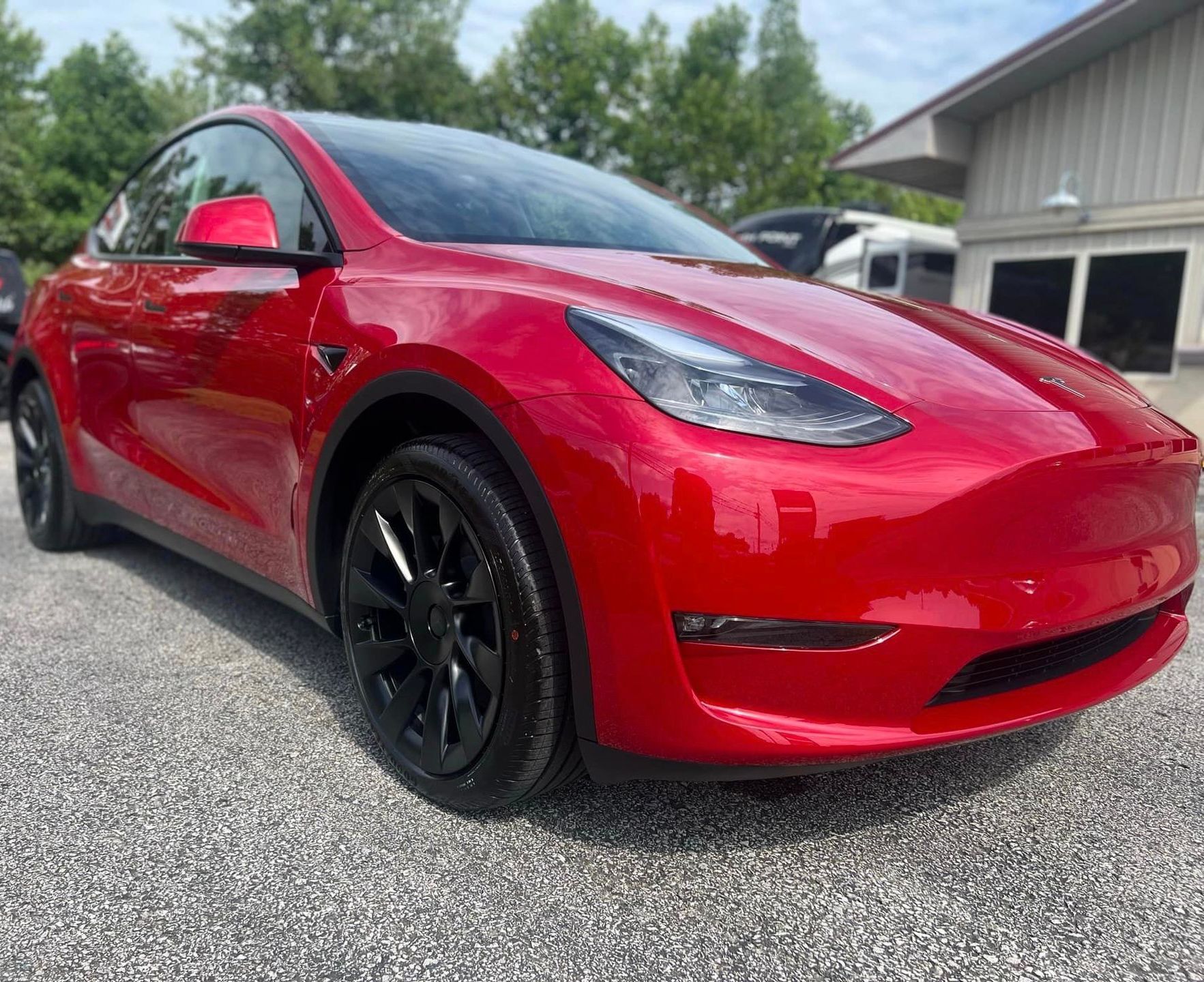 Red Tesla Model Y parked outdoors with black wheels, under a blue sky.