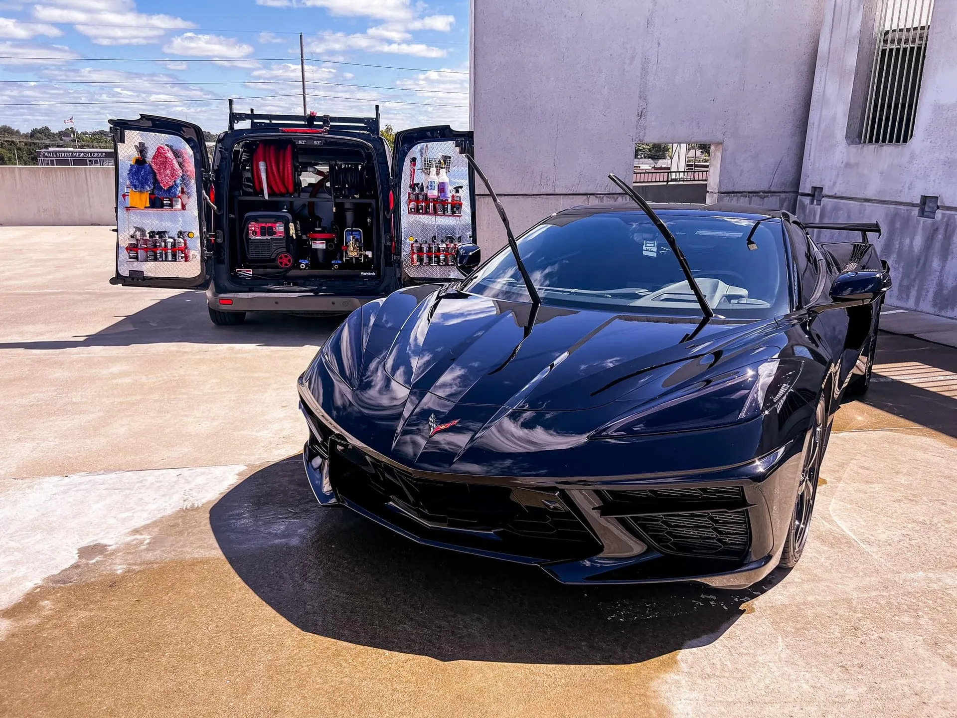 Black Corvette parked next to a mobile detailing van on a sunny rooftop.