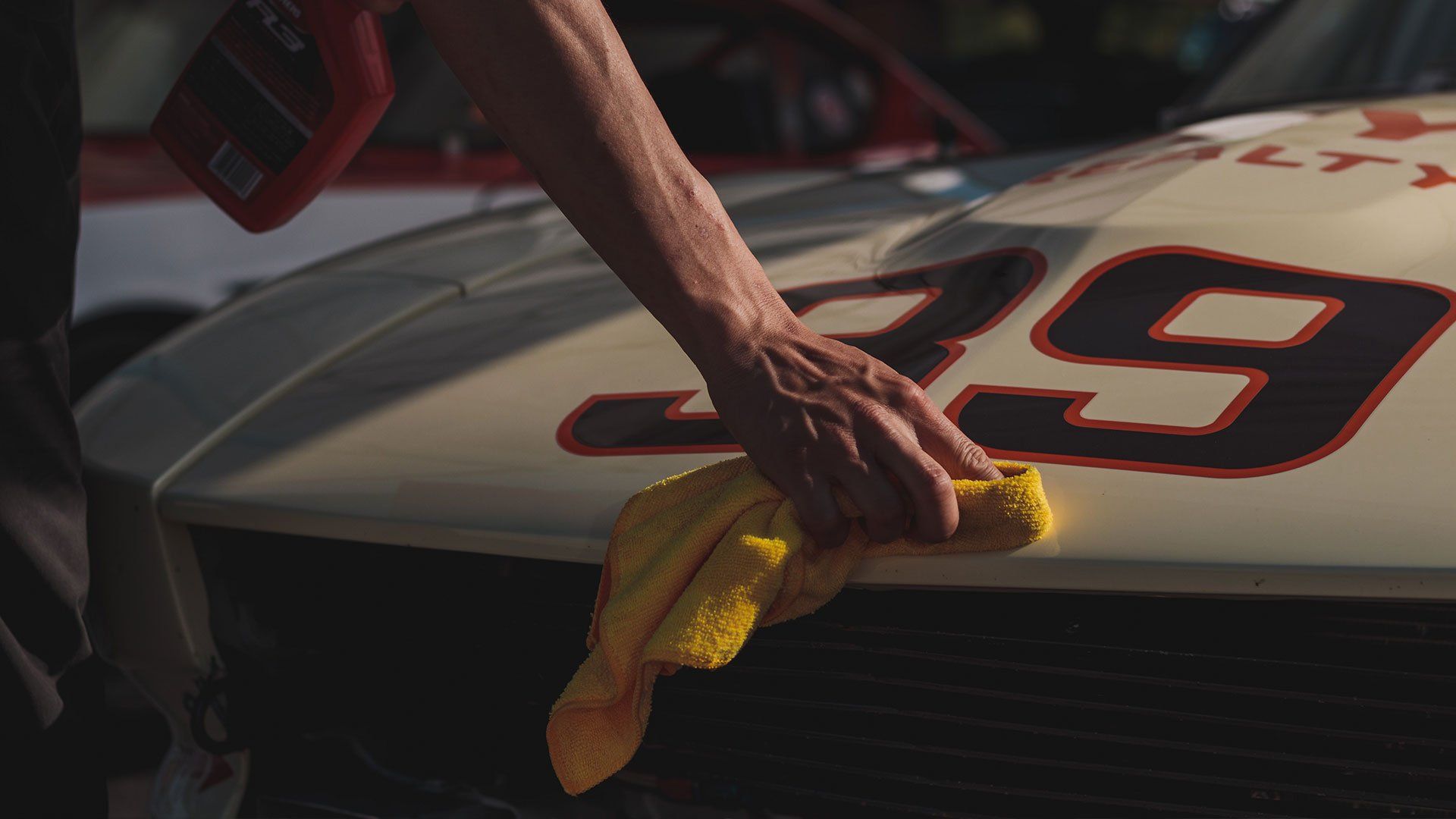 Person wiping the hood of a racing car with a yellow cloth. Car has the number 29 in red.