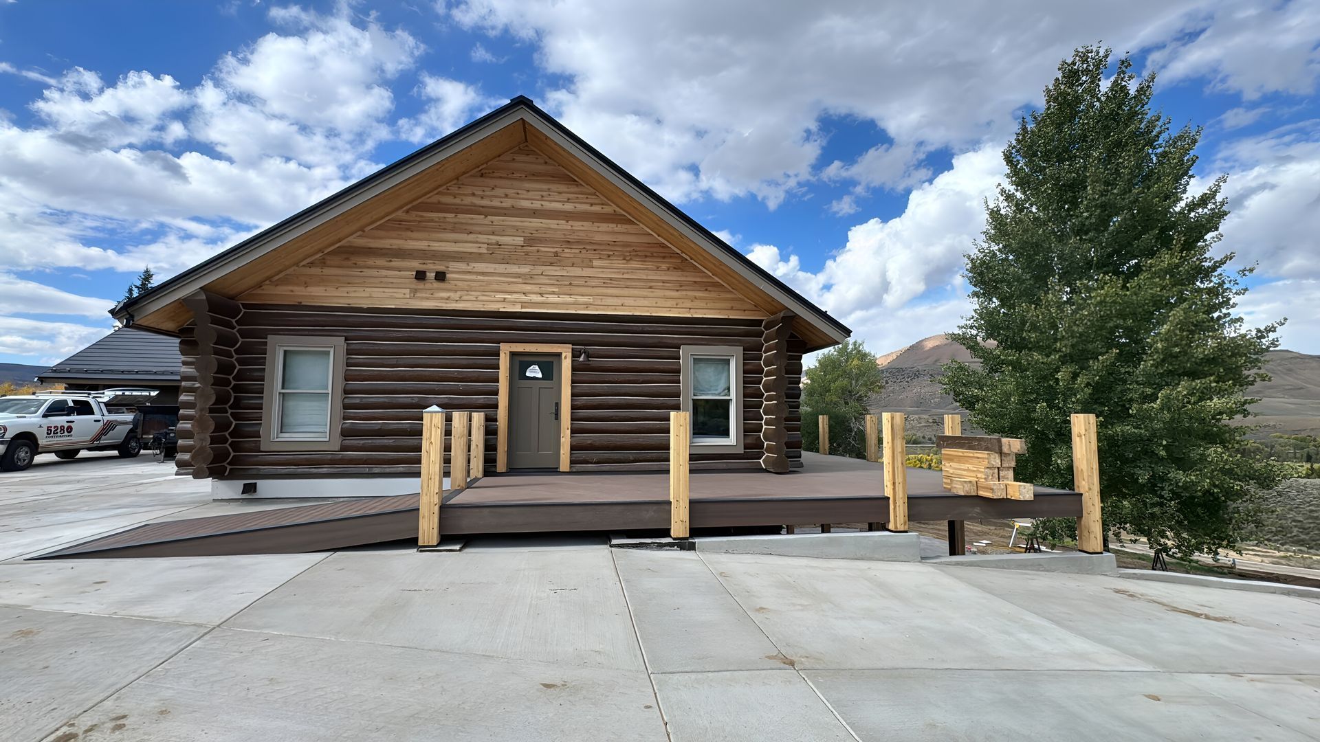Log cabin-style building with wooden porch and concrete parking area under a blue sky