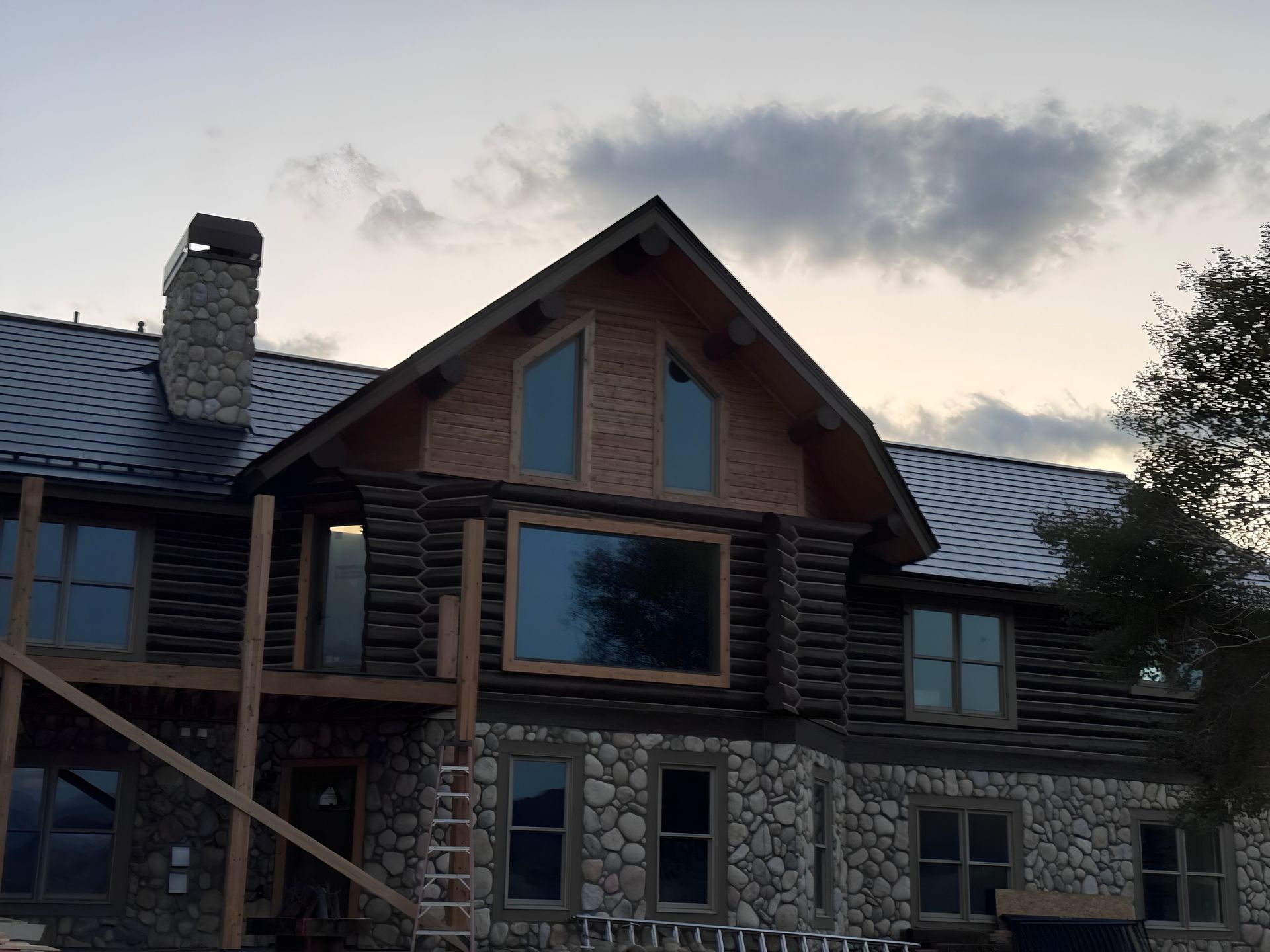 Stone and wood house with a steep roof at dusk, framed by a cloudy sky.