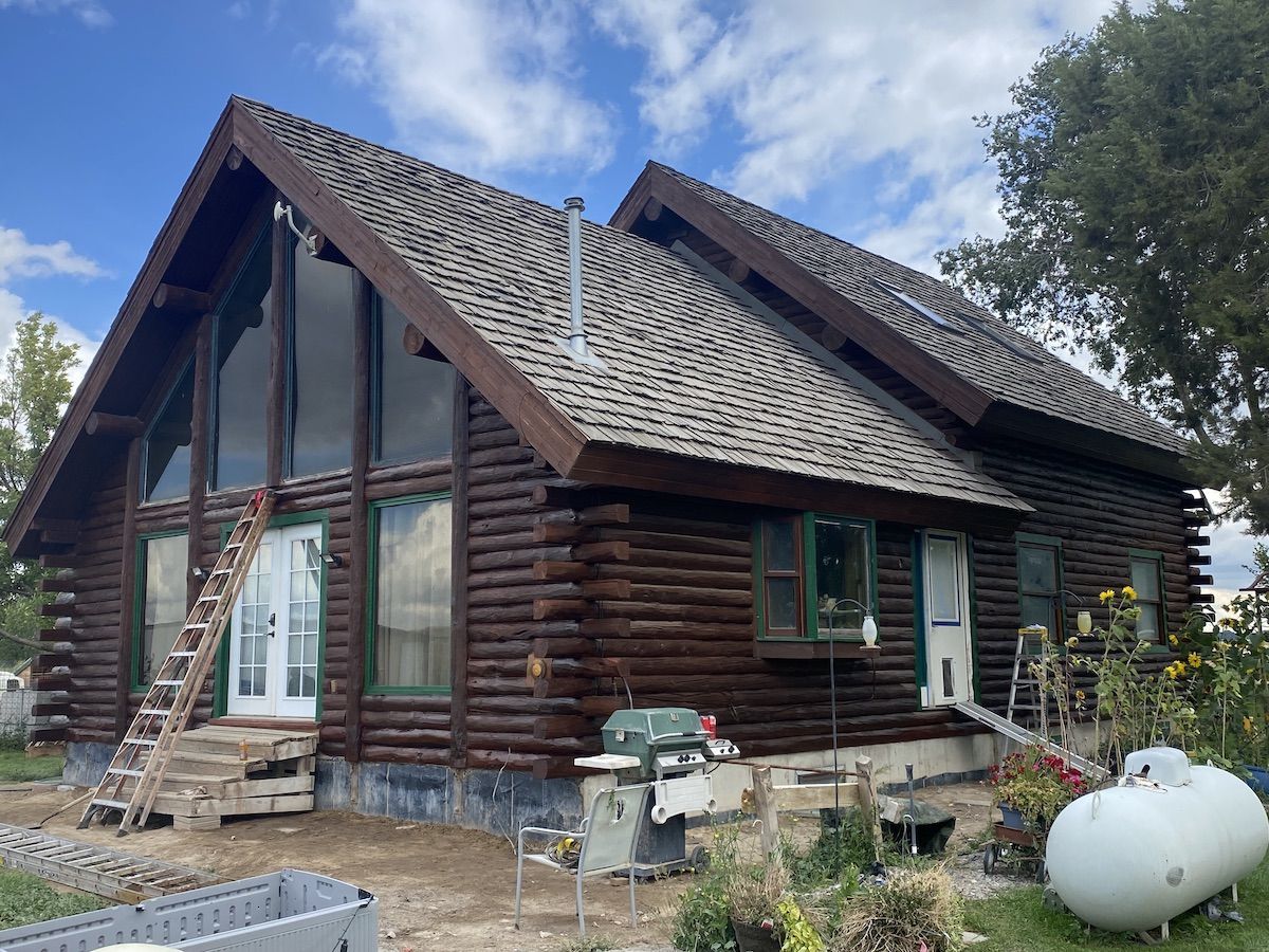 Rustic log cabin with steep roof, large windows, and construction materials in the yard.