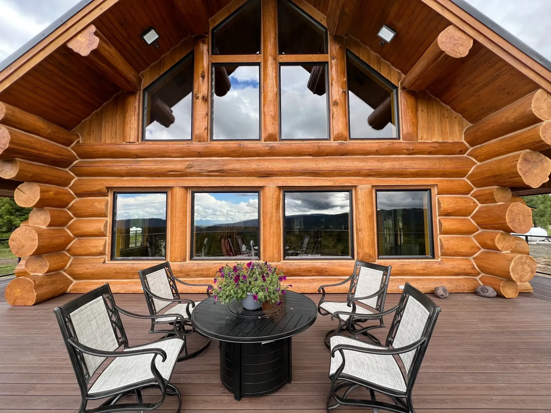Log cabin porch with four chairs around a round table and flower centerpiece under a wooden overhang