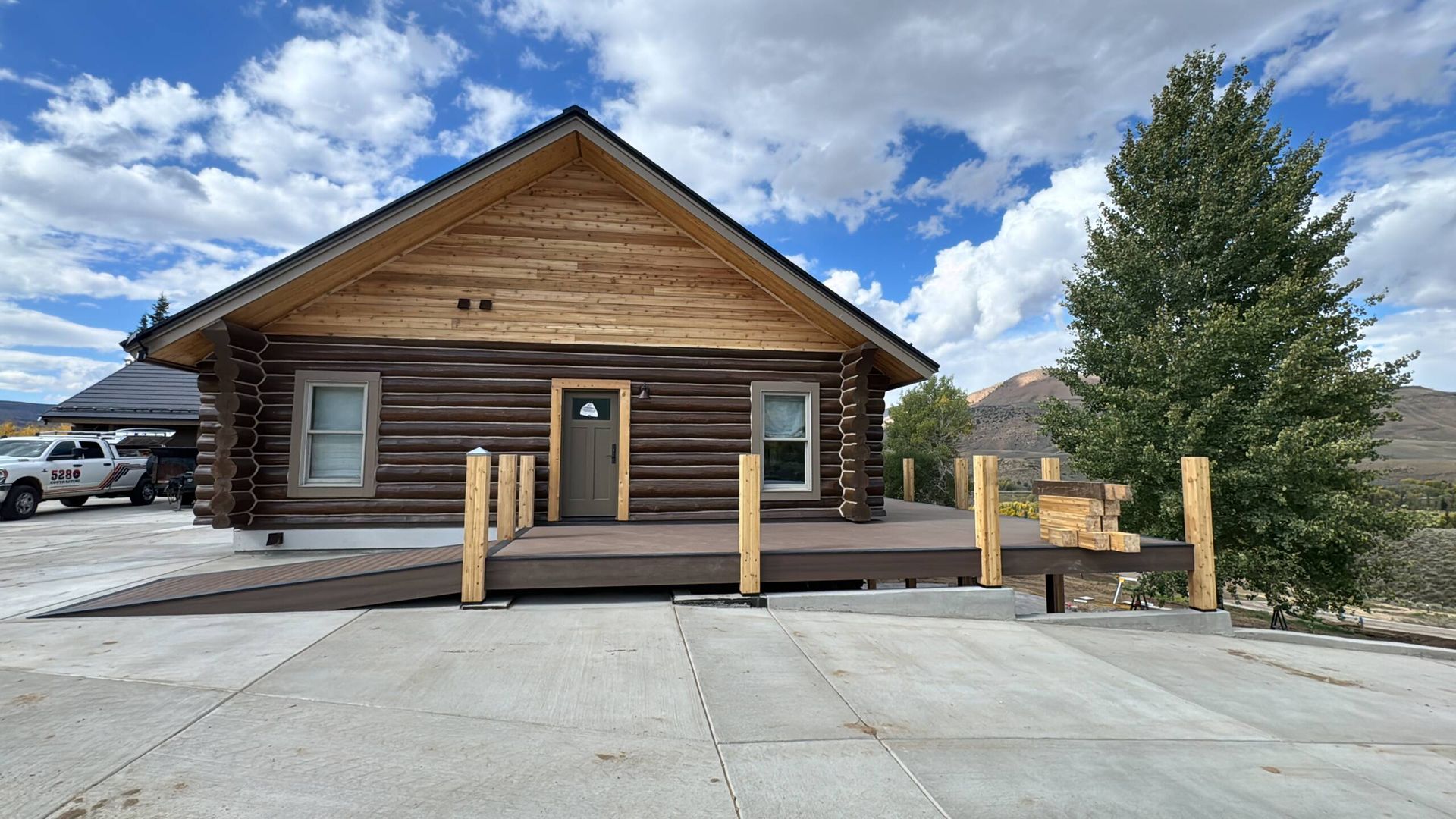 Rustic log cabin with wooden porch and posts, front view under a cloudy blue sky