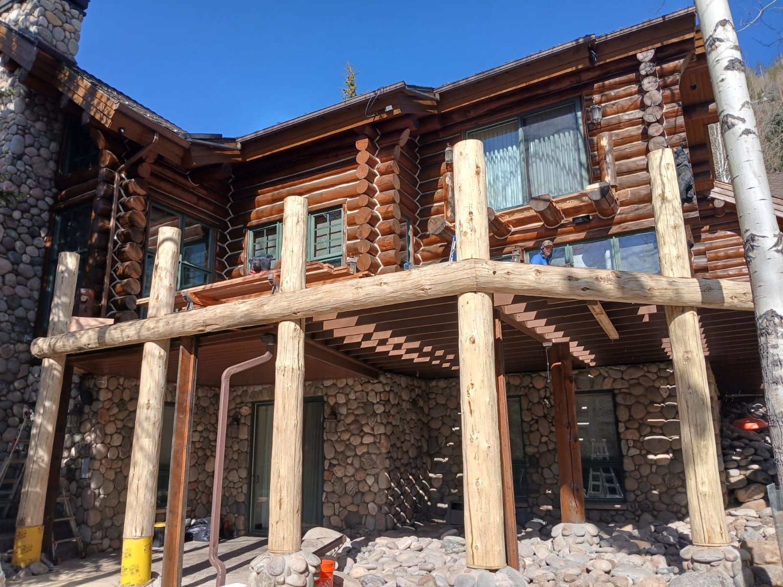Rustic log cabin under construction with wooden beams and stone walls on a sunny day