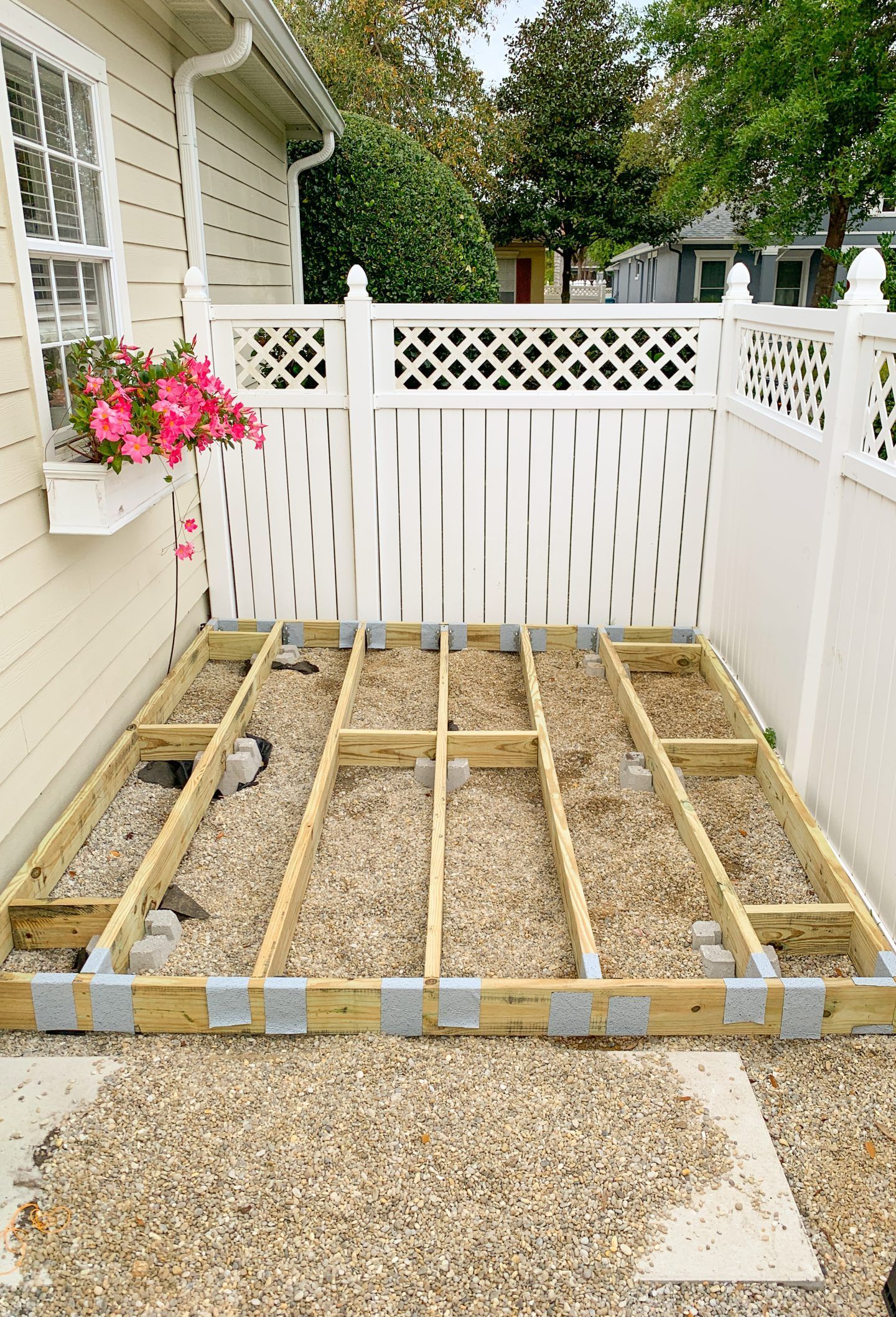 Wooden deck frame under construction beside a white lattice fence and pink flowers