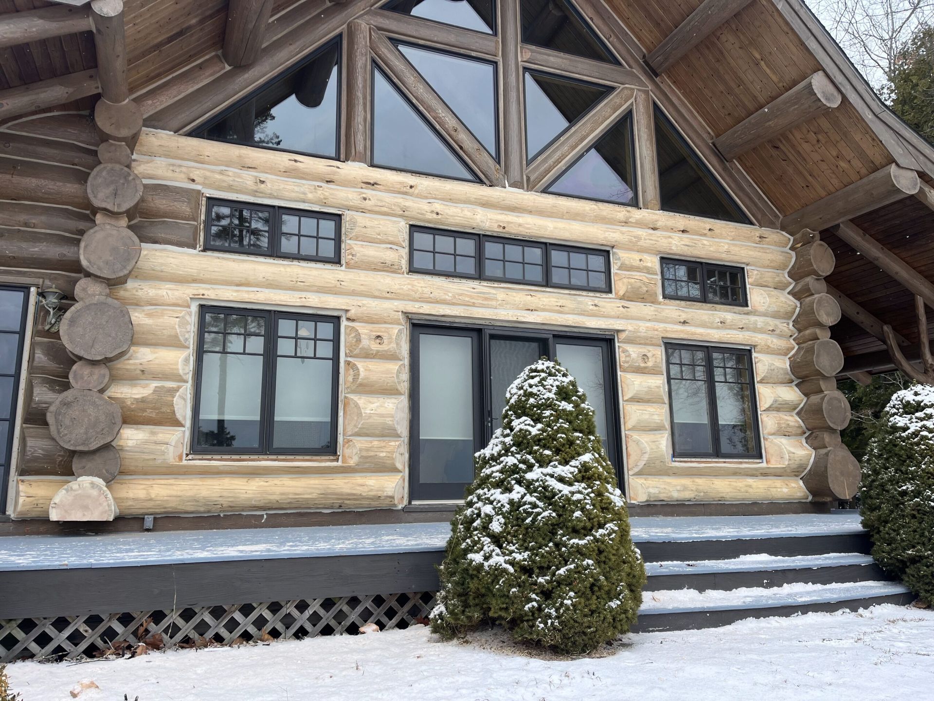 Snowy log cabin with large windows and steps at the entrance