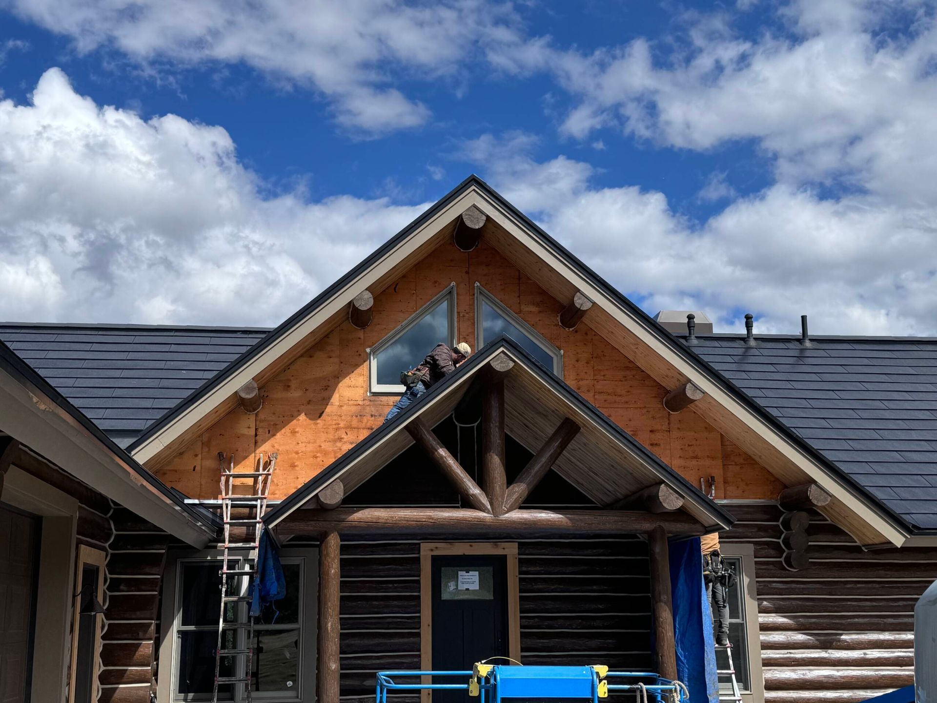 Front view of a rustic log cabin with a wooden gable and partly cloudy blue sky