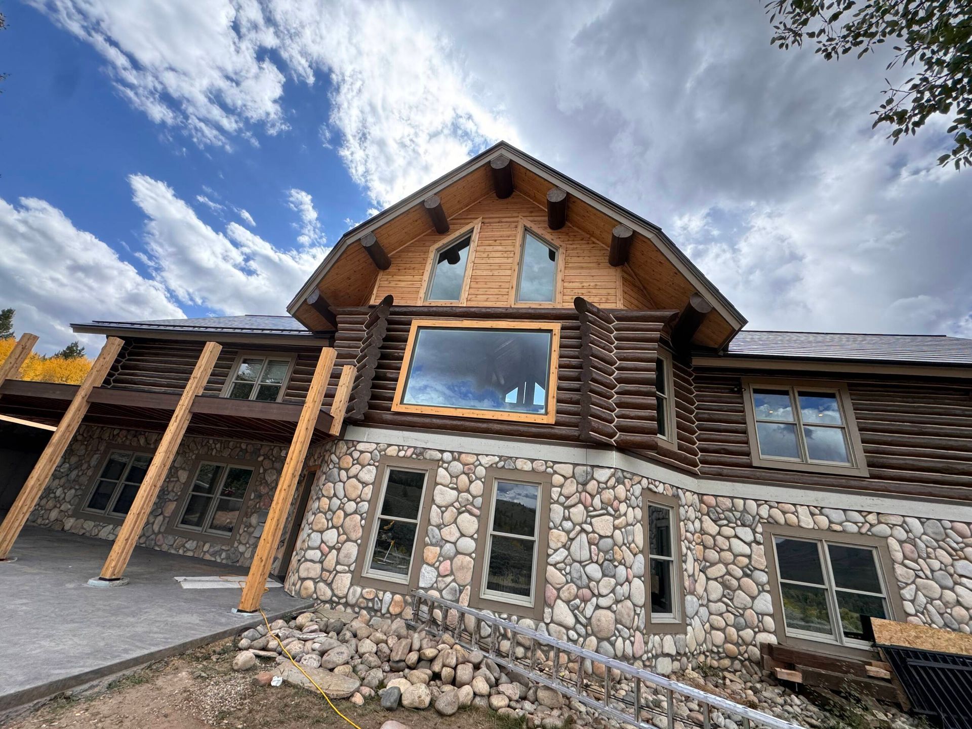 Log cabin-style stone and wood house with large windows under a cloudy blue sky