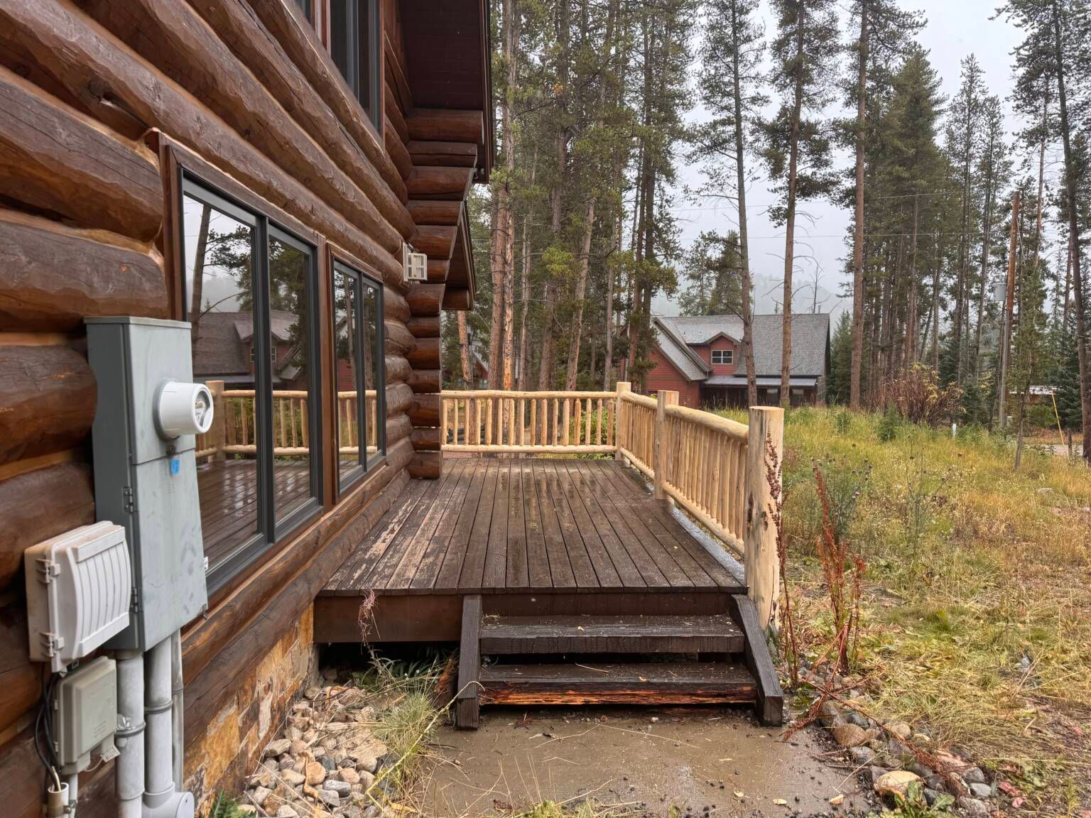 Log cabin deck with wooden steps, railing, and pine forest view in the background