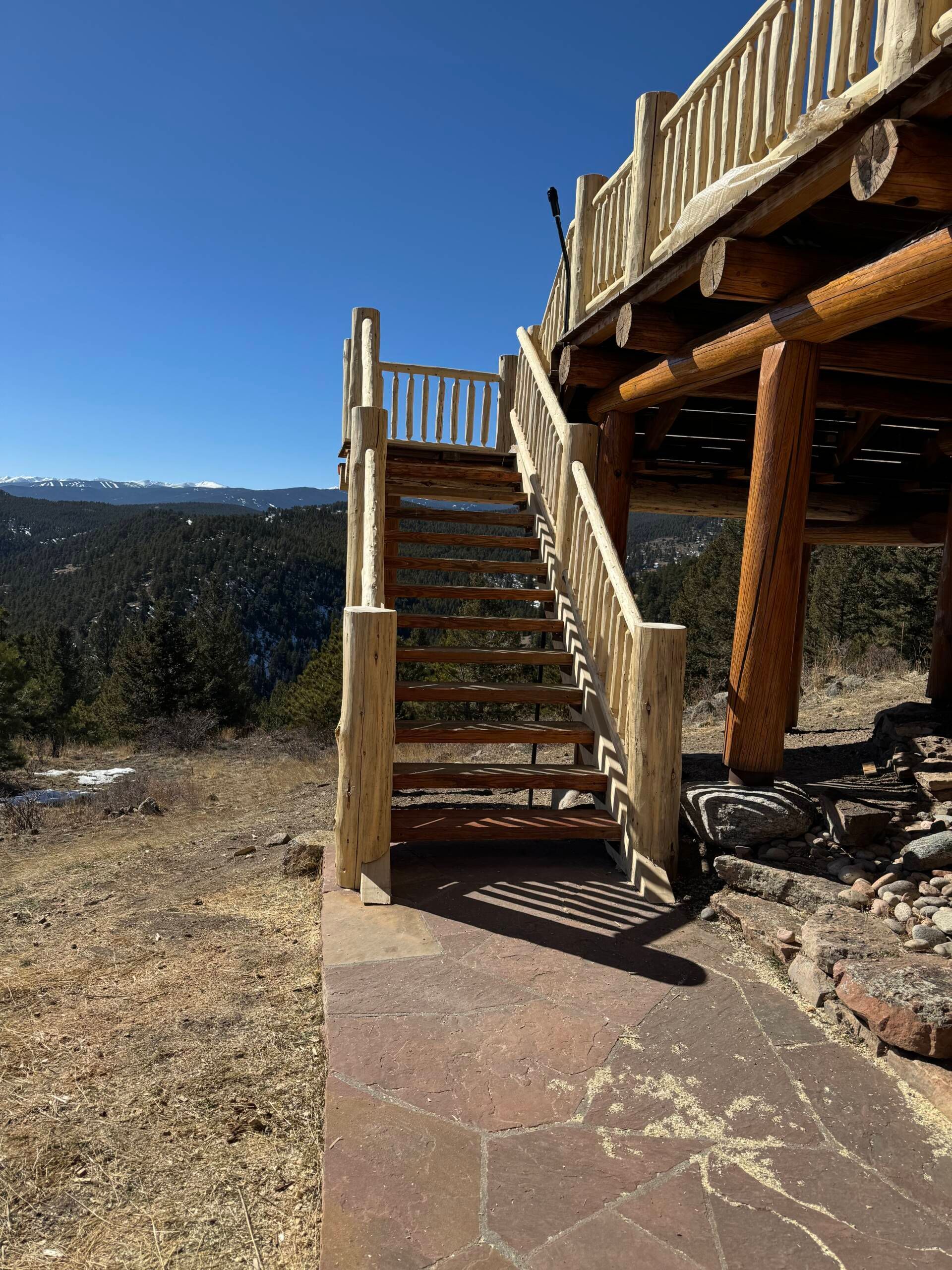 Wooden stairs leading to an elevated deck overlooking a sunny desert landscape under a blue sky