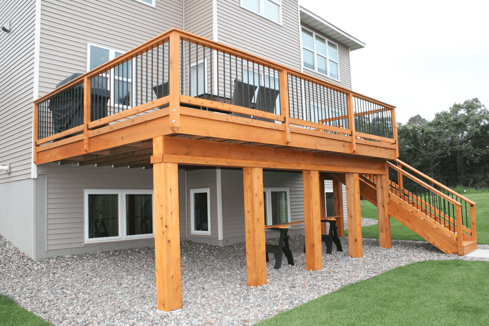 Wooden deck and staircase on a house exterior with gray siding and gravel yard.