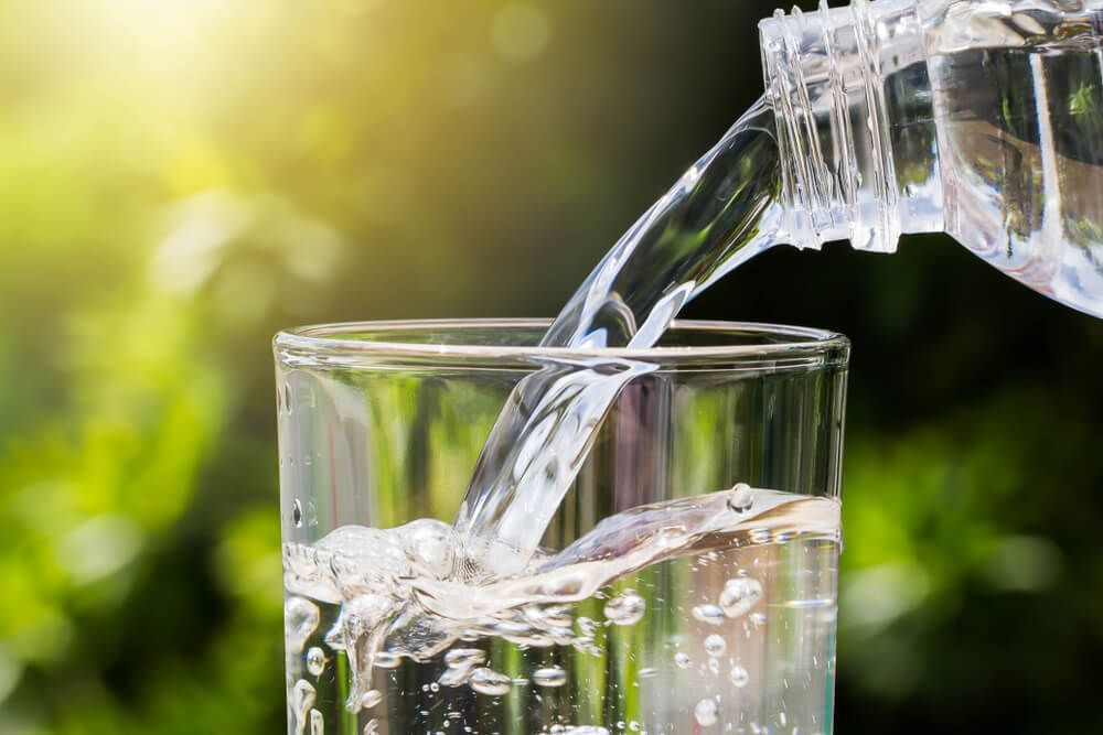 Water Is Being Poured Into A Glass From A Bottle — Eureka Water & Filtration In Mount St John, QLD