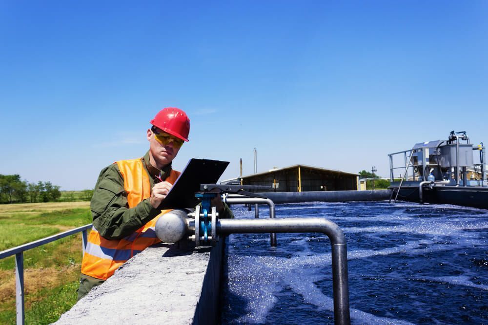 A Man In A Hard Hat Is Looking At A Clipboard In A Water Treatment Plant — Eureka Water & Filtration In Mackay, QLD