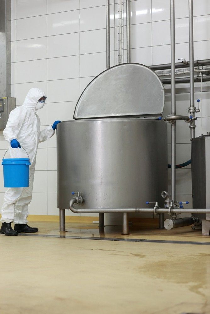 A Man In A Protective Suit Is Cleaning A Stainless Steel Tank In A Factory — Eureka Water & Filtration In Cairns, QLD