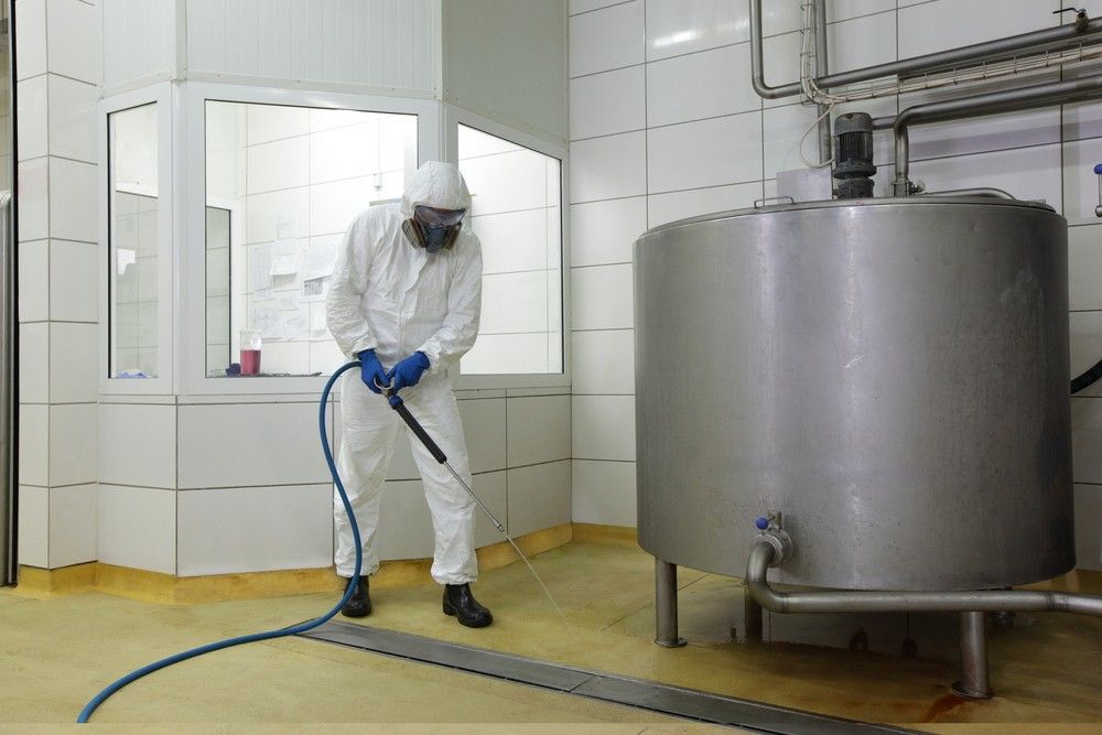 A Man In A Protective Suit Is Cleaning A Tank With A Hose — Eureka Water & Filtration In Mount Isa, QLD