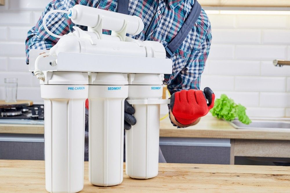 A Man Is Fixing A Water Filter In A Kitchen — Eureka Water & Filtration In Mackay, QLD