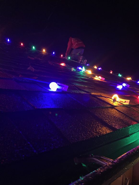 A person is standing on a roof with christmas lights on it.