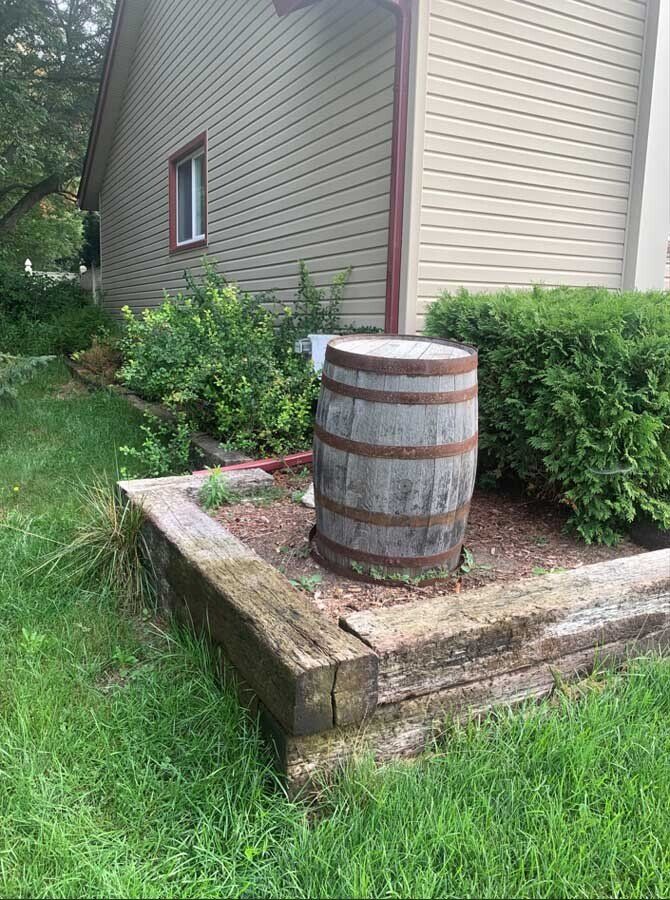A wooden barrel is sitting in the grass in front of a house. landscape 