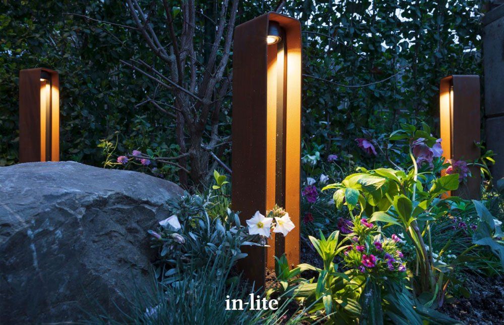 A brick walkway surrounded by tall grass and flowers. landscape lighting