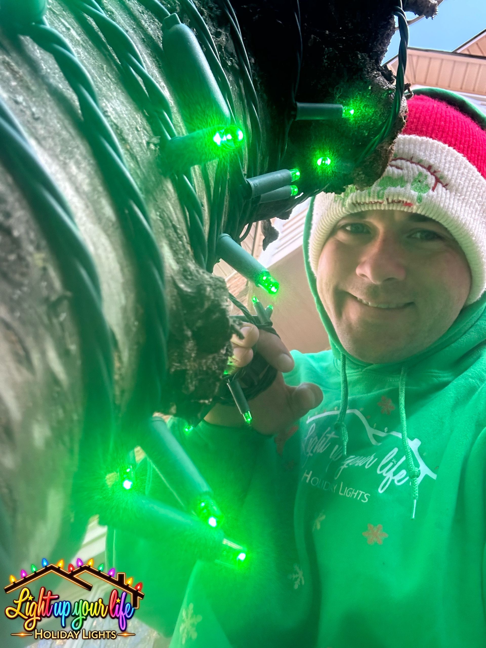 green mini lights on a tree with a certified installer smiling. 