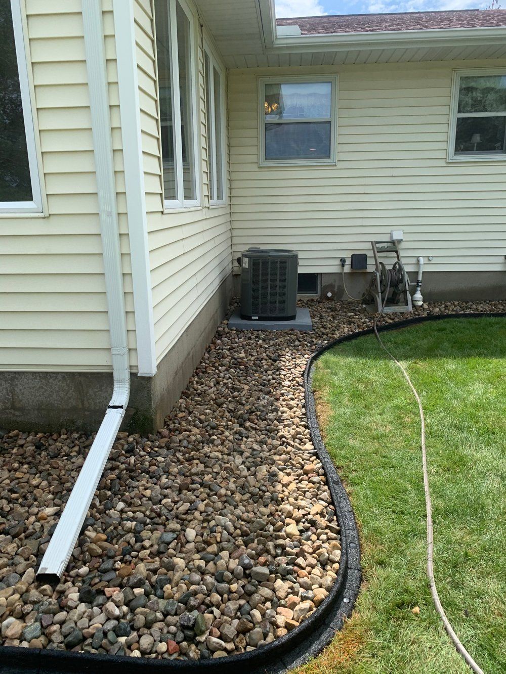A large piece of black tarp is laying on the grass next to a house. weed barrier