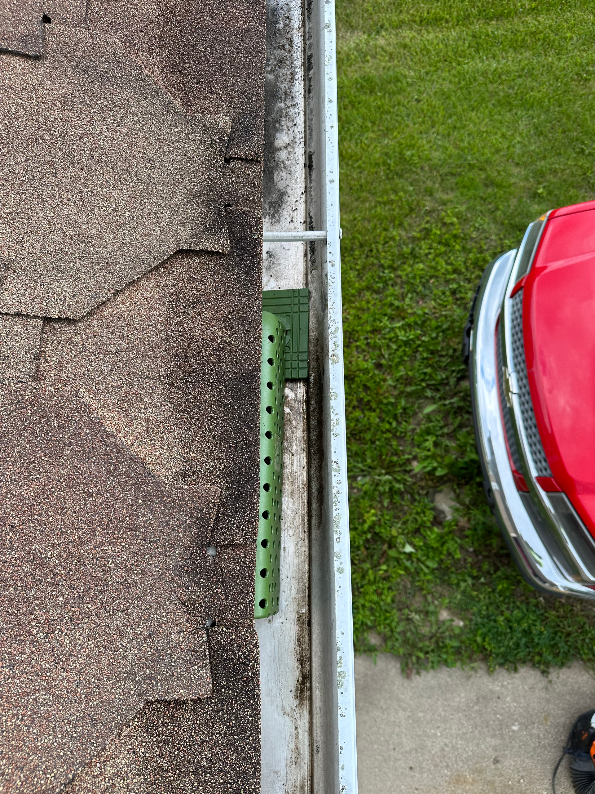Roof edge with a gutter; green bracket and red car visible. Gutter Cleaning
