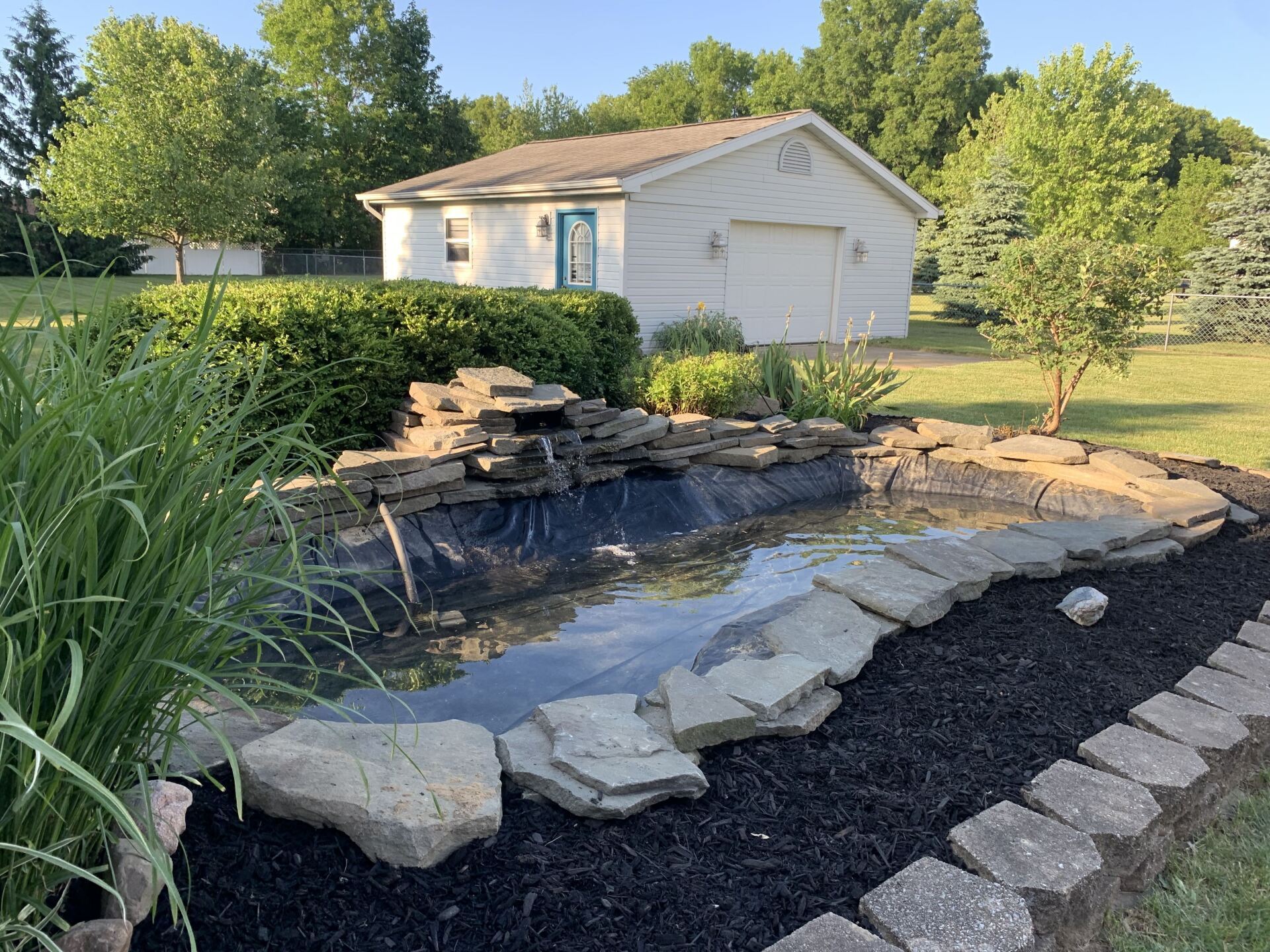 A pond with a waterfall in front of a house. LANDSCAPE