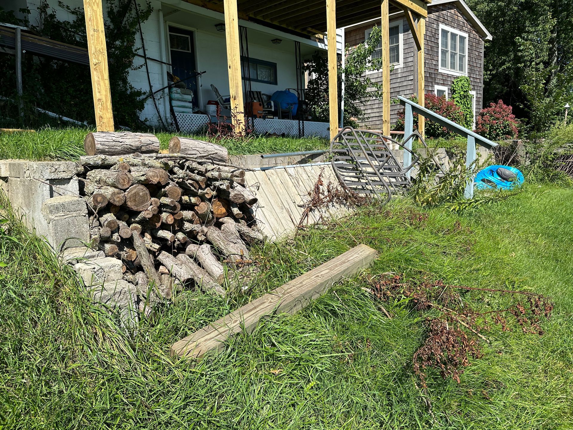 A pile of logs is sitting in the grass in front of a house.