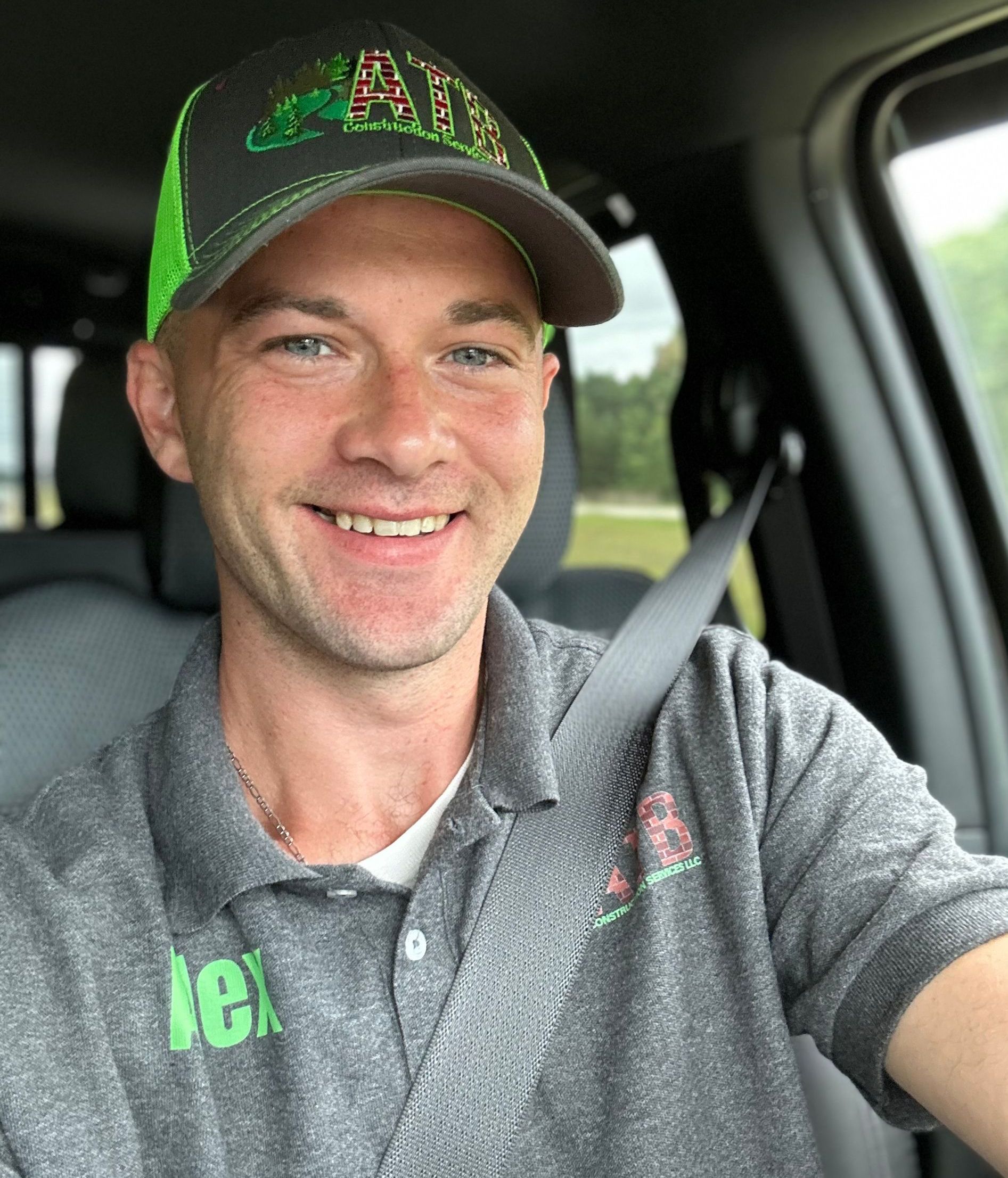 A man is sitting in a car wearing a hat and smiling.