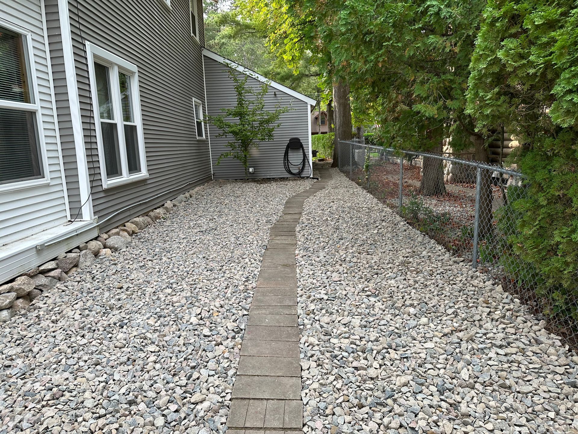 A gravel path leading to a house with a chain link fence. stepping stones