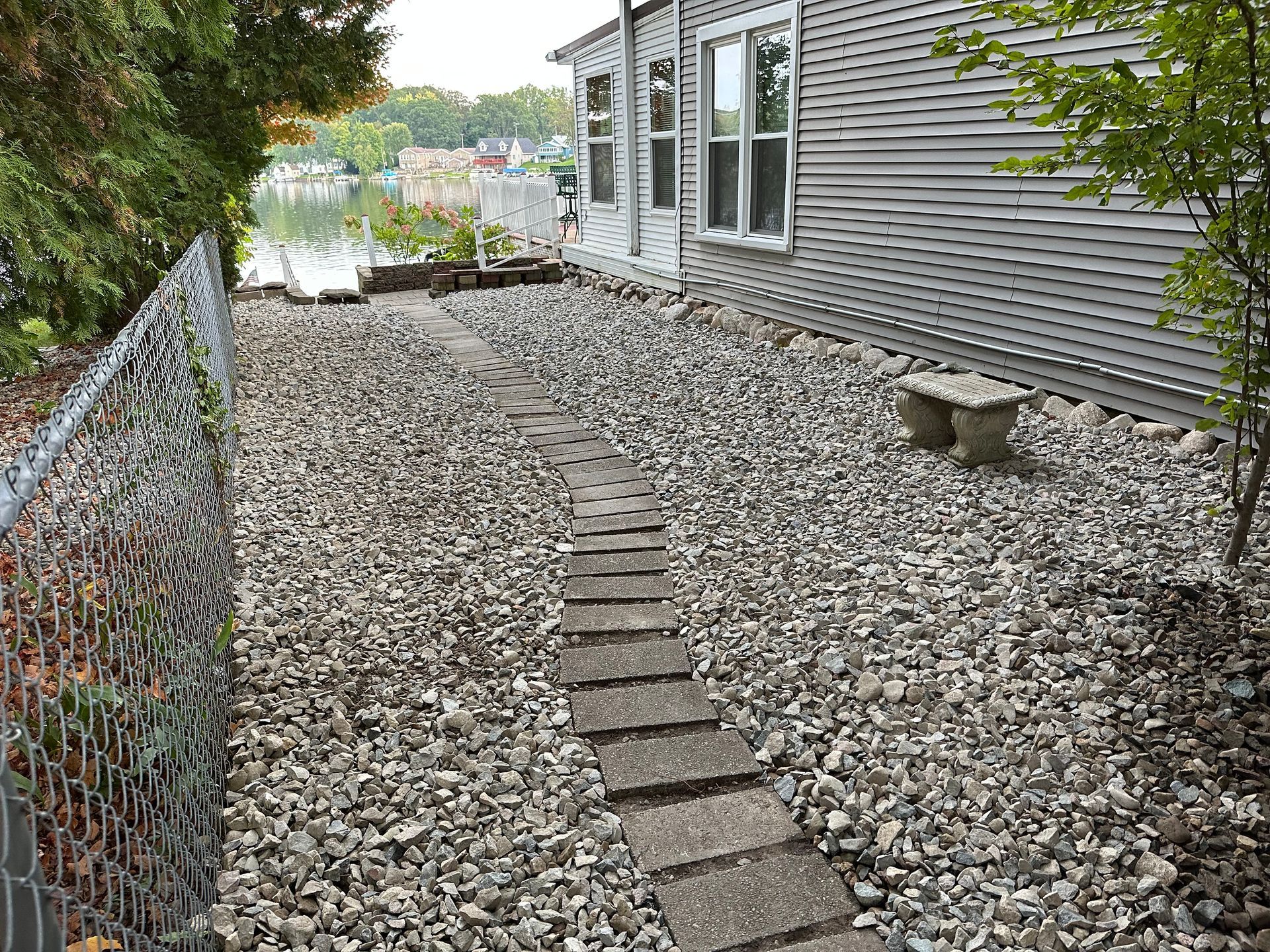 A path leading to a house surrounded by rocks and a chain link fence.