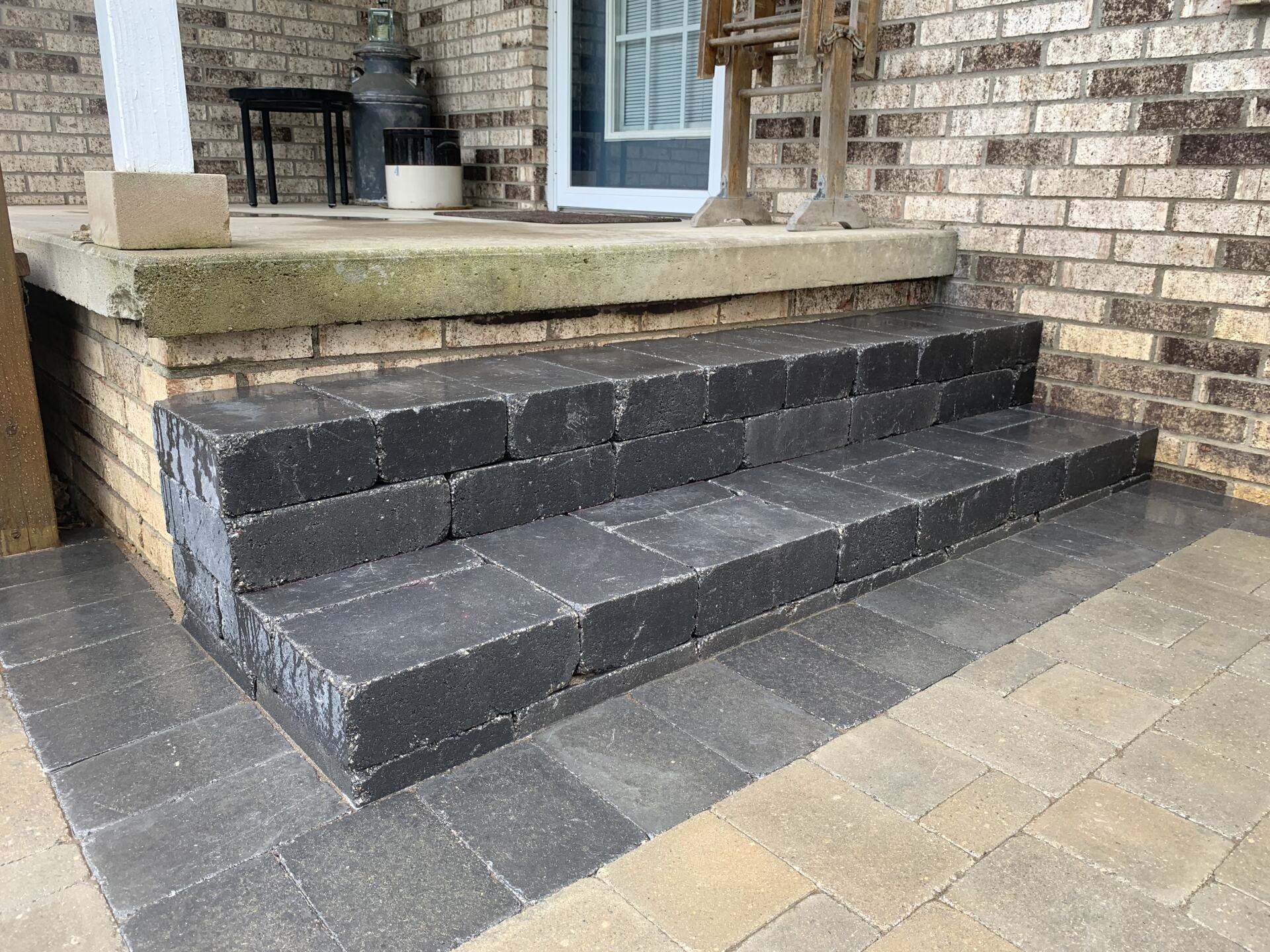A set of steps leading up to a porch of a brick house. brick pavers