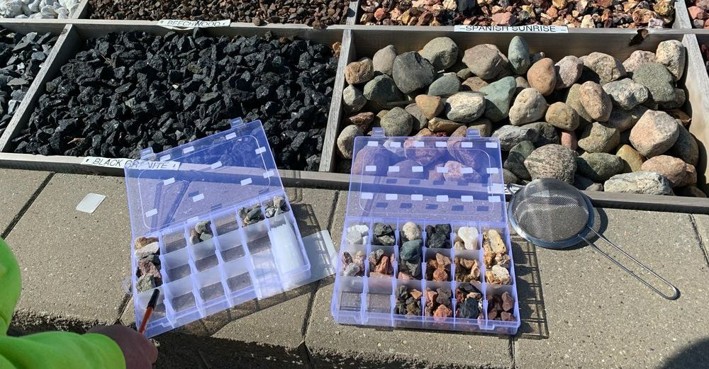 Two plastic boxes filled with rocks are sitting on a sidewalk. ROCK INSTALLATION 