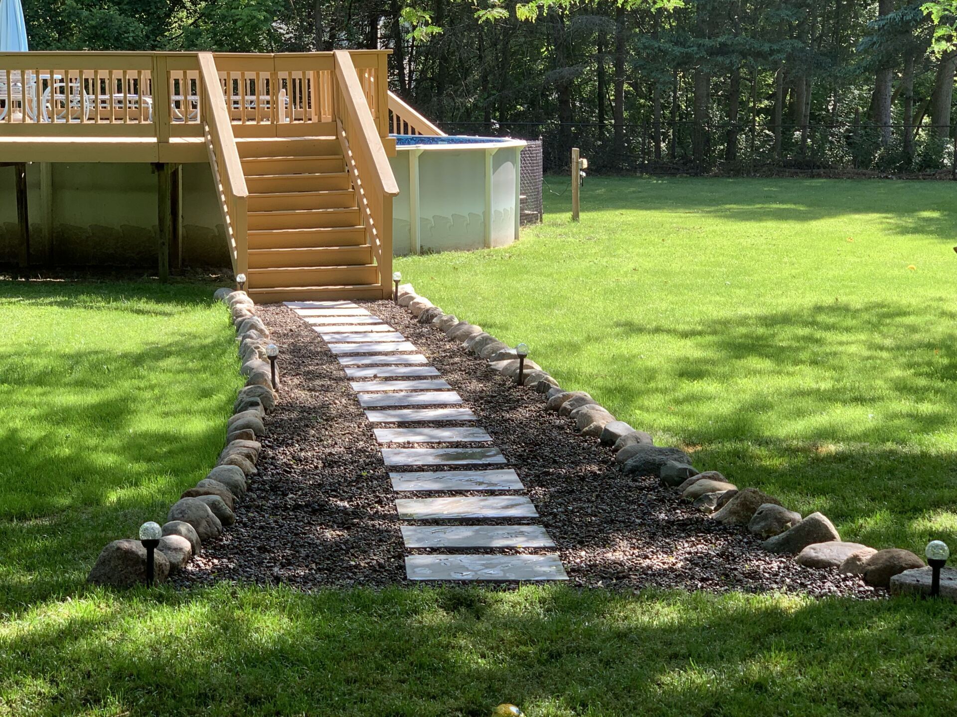A walkway leading to a deck in a backyard. mulch, stepping stones.
