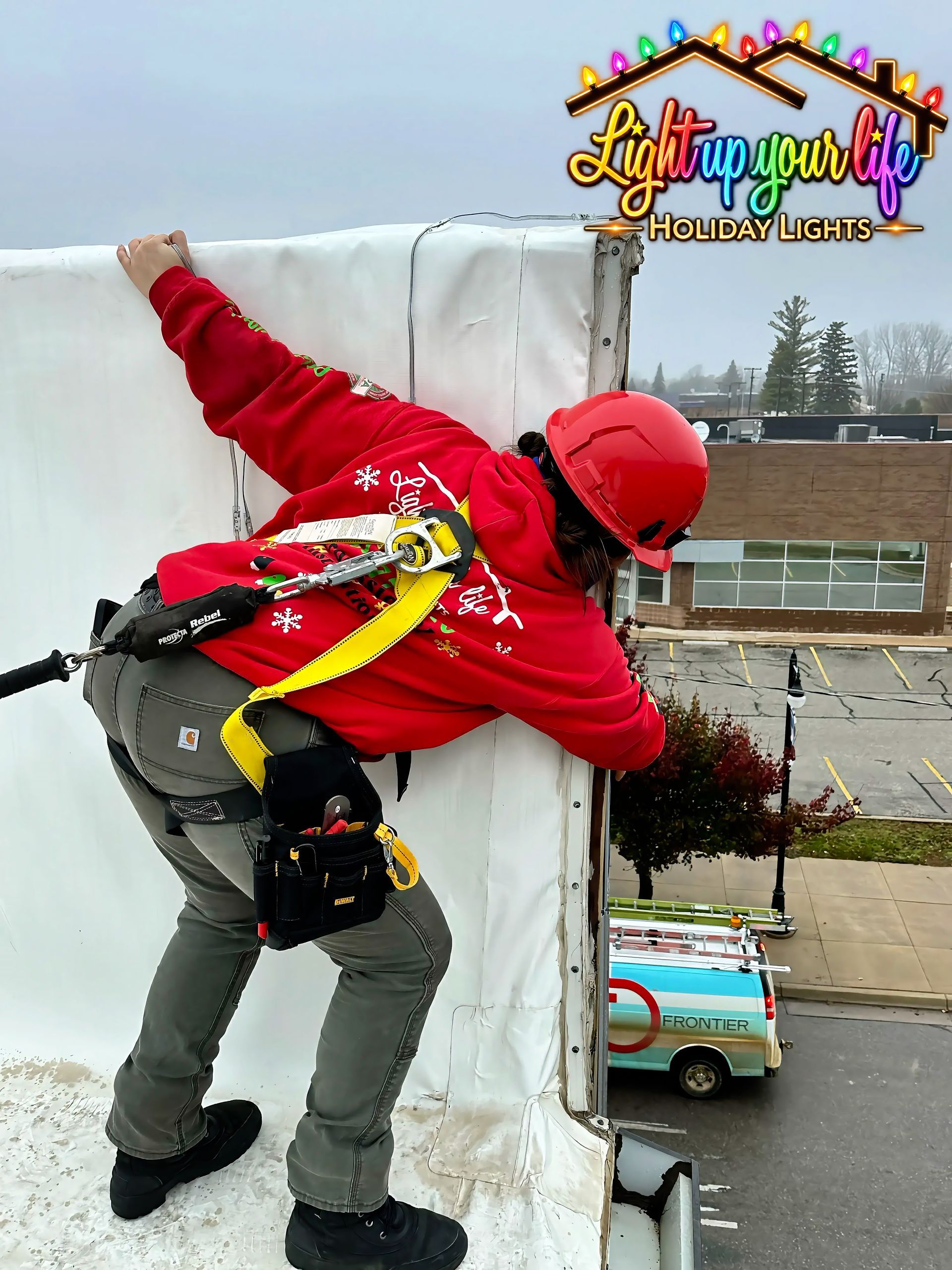 Certified and trained light installer with a harness on that is anchored to the roof on a downtown michigan building for safety. 