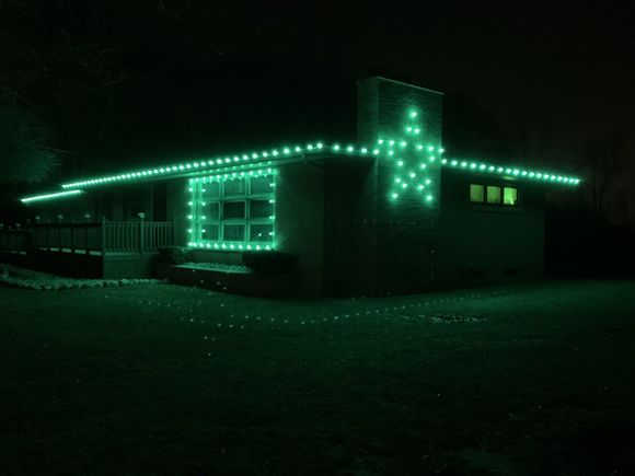A house is decorated with green christmas lights at night.