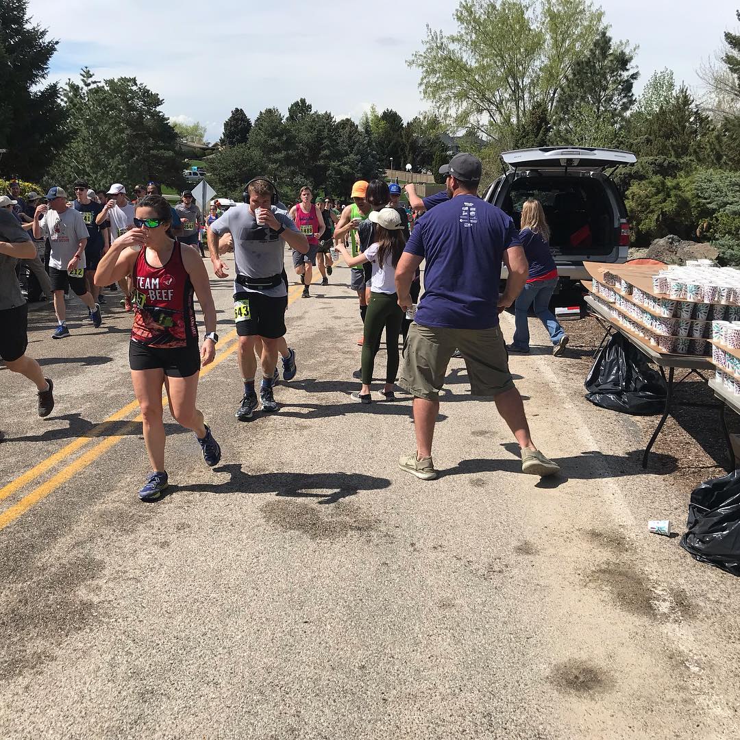 Runners in a race on a road with a water station and volunteers.