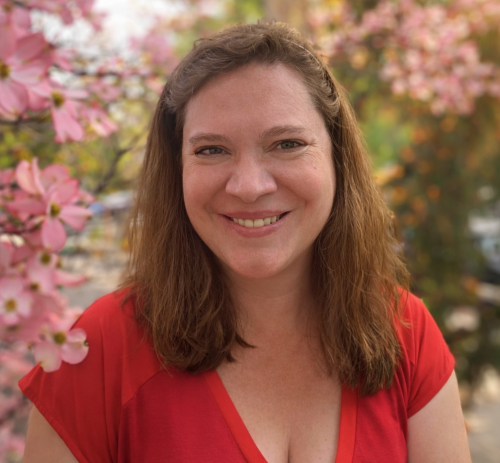 Woman in a red top smiles in front of a blooming pink dogwood tree.