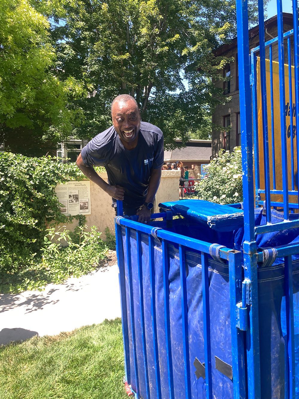 Man stands by a blue dunk tank, smiling. Outdoor setting, sunny day.