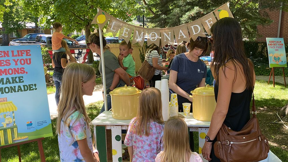 Lemonade stand in a park. People buying lemonade from a stand decorated with lemons. Sign says