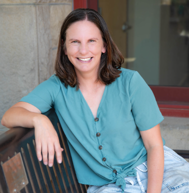Woman in green shirt smiles outdoors, seated on a bench, with a green background.
