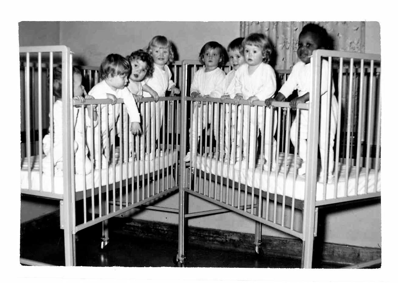 Group of babies in cribs, looking at camera.