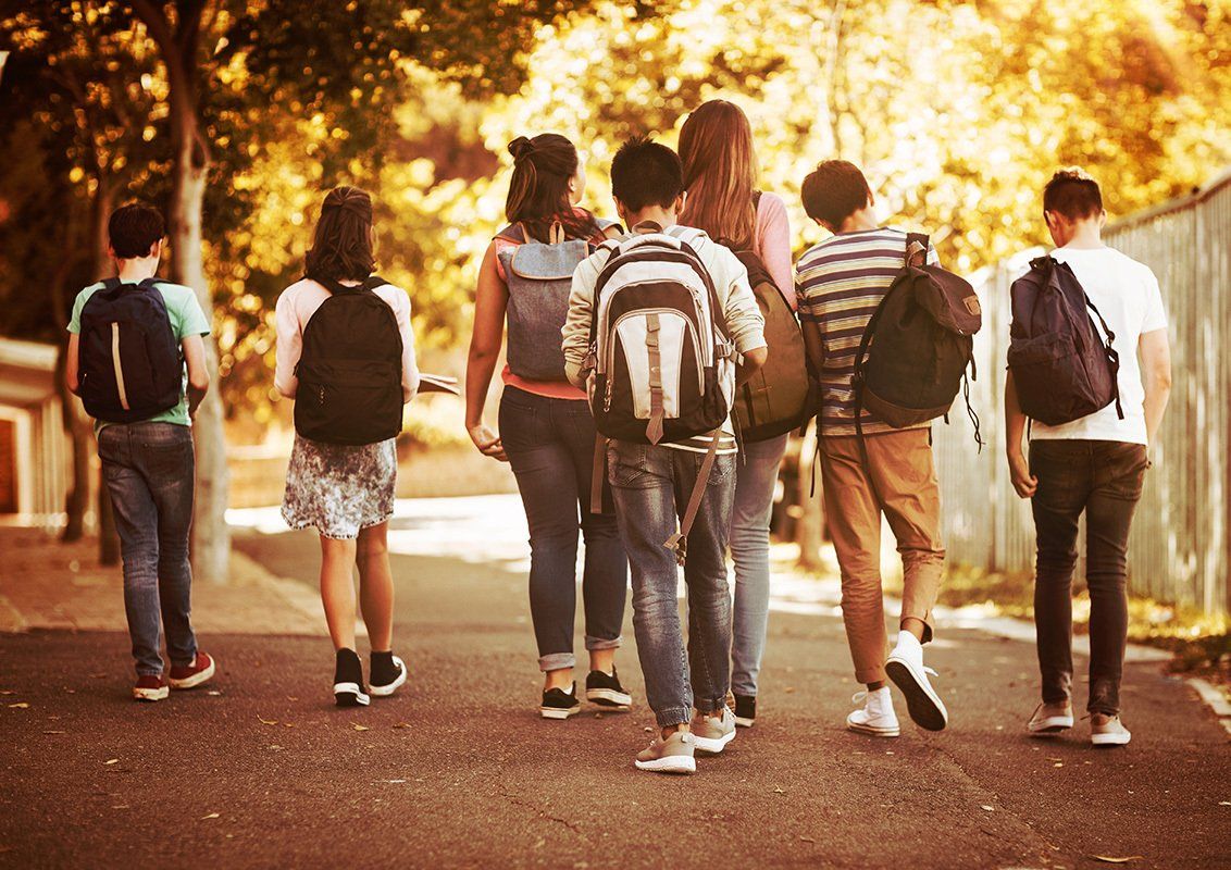 Group of students walking on a sidewalk, carrying backpacks, sunny outdoor setting.