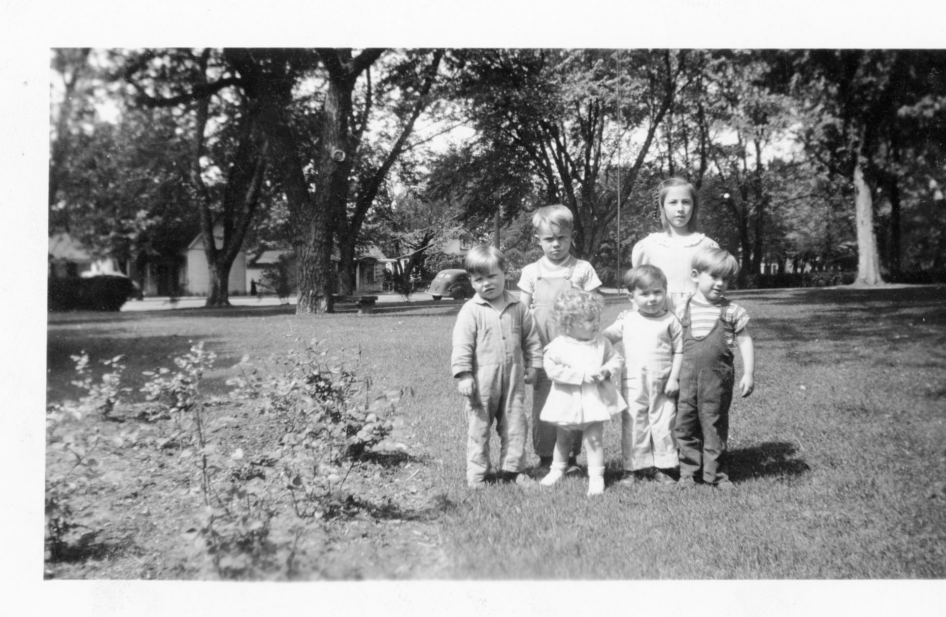 Group of six children standing in a grassy yard in front of a house.
