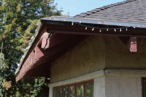 Brown-roofed house corner with decorative eaves, brown trim, and string of white lights.
