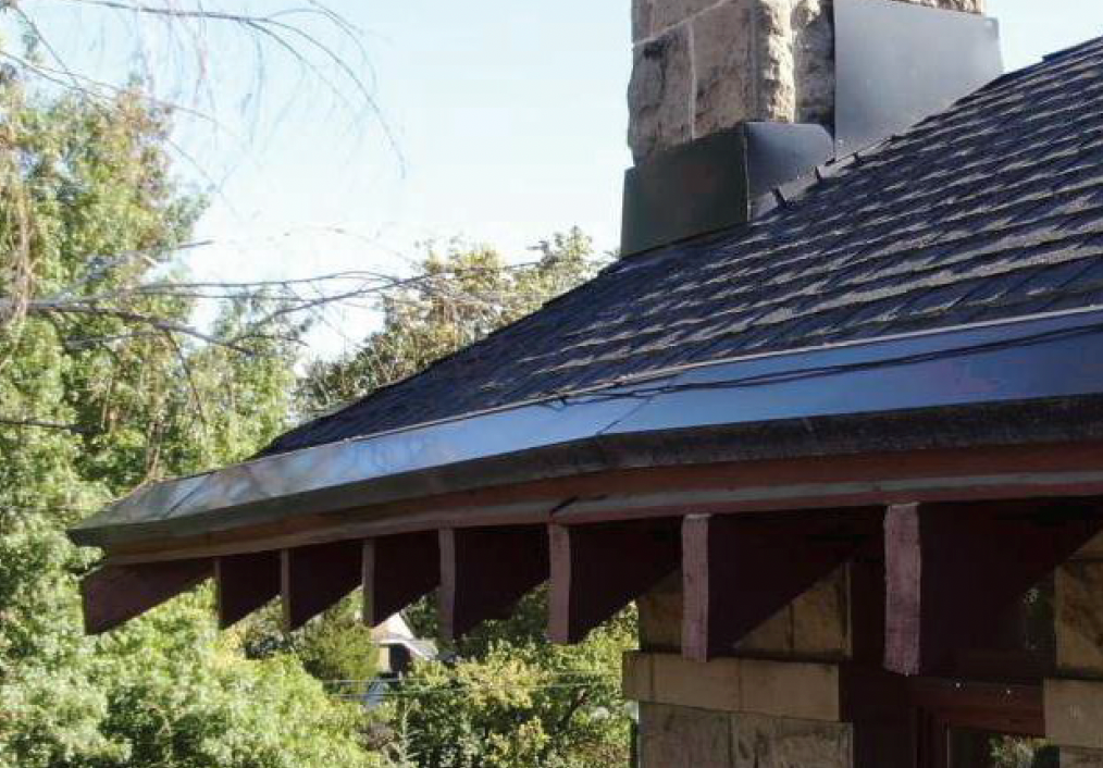 Roof of a building with dark shingles, a metal gutter, and decorative wooden brackets.