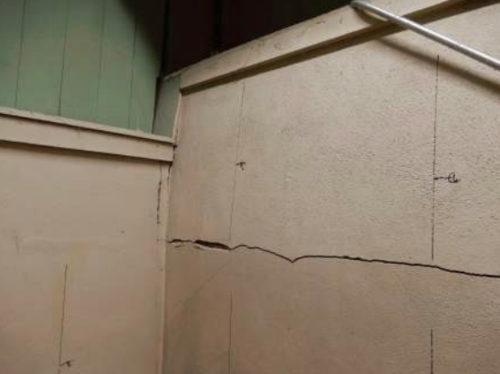 Beige wall with a horizontal crack and vertical markings in the corner. Green wall in the background.