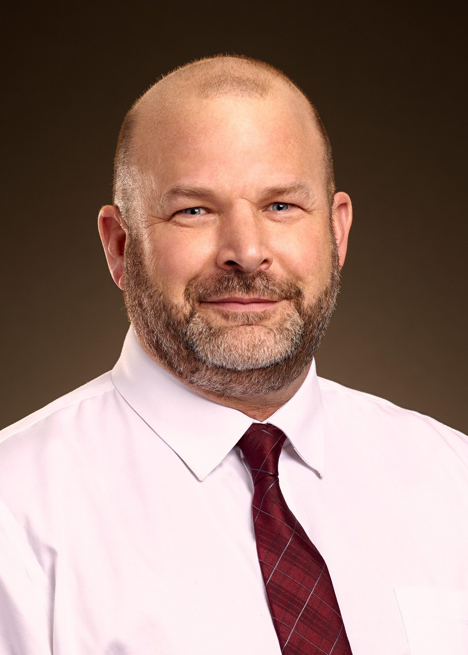 Man with a bald head and beard wearing a light pink shirt and burgundy tie, smiling.